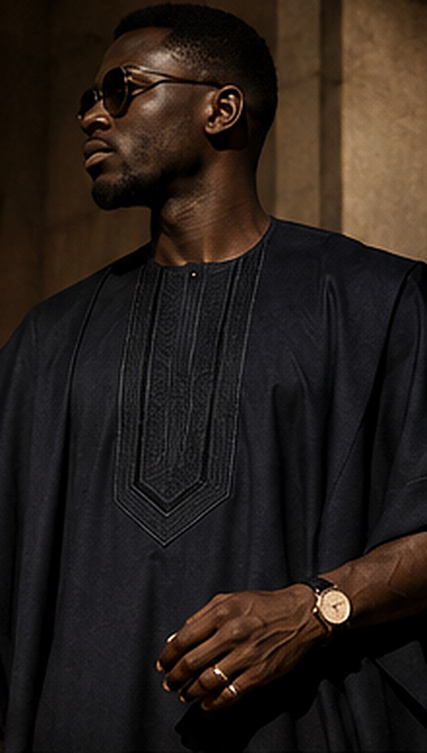 A man wearing a black embroidered agbada in warm architectural light